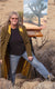 Marcia Geiger wearing a long jacket standing in front of a painting of a Joshua tree landscape that's resting on an easel
